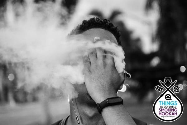 Man blowing hookah smoke through hand black and white